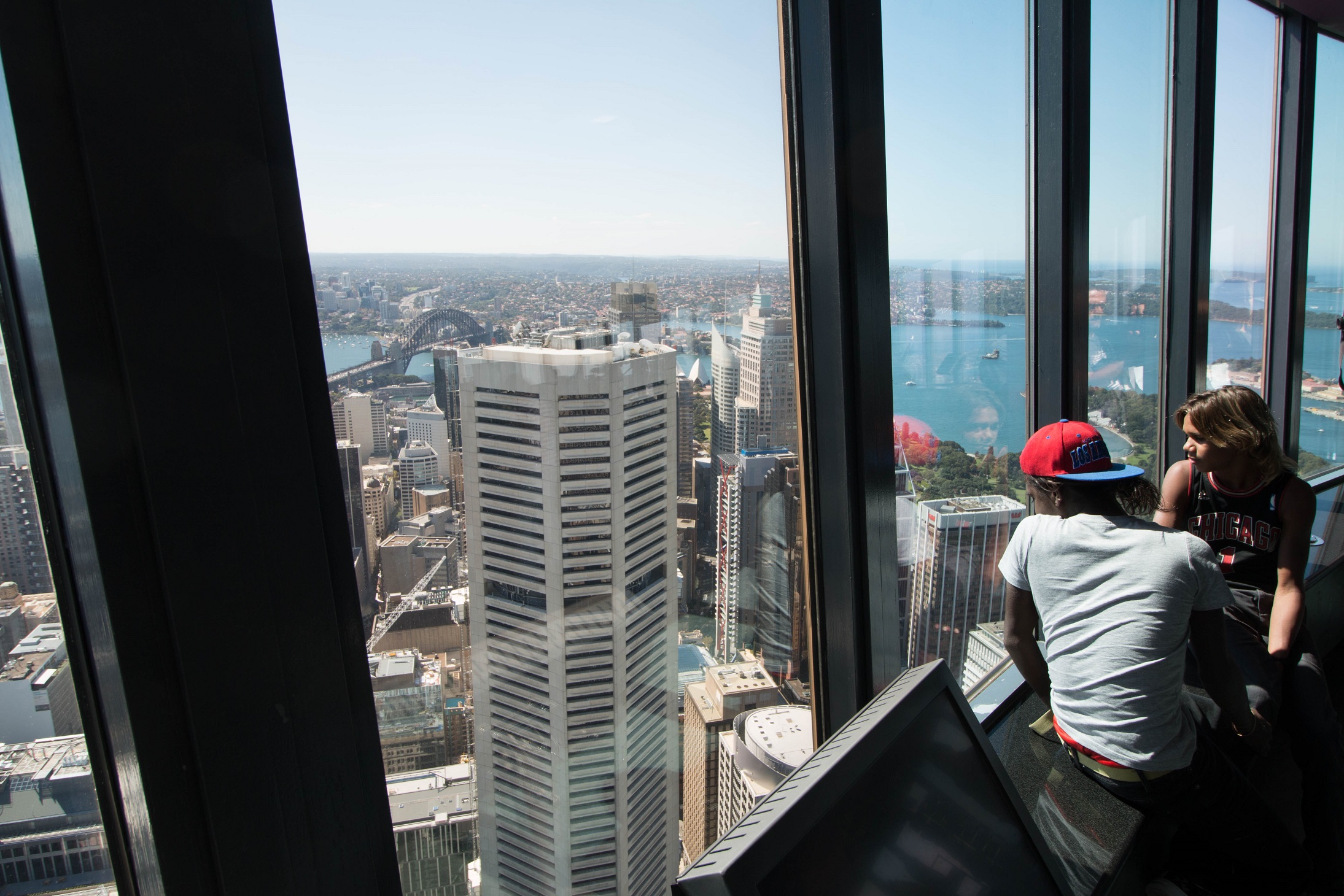 Lester Gumbula and Nehemiah Farrell inside Centre Point Tower, Sydney, looking out towards the Harbour Bridge (on left)