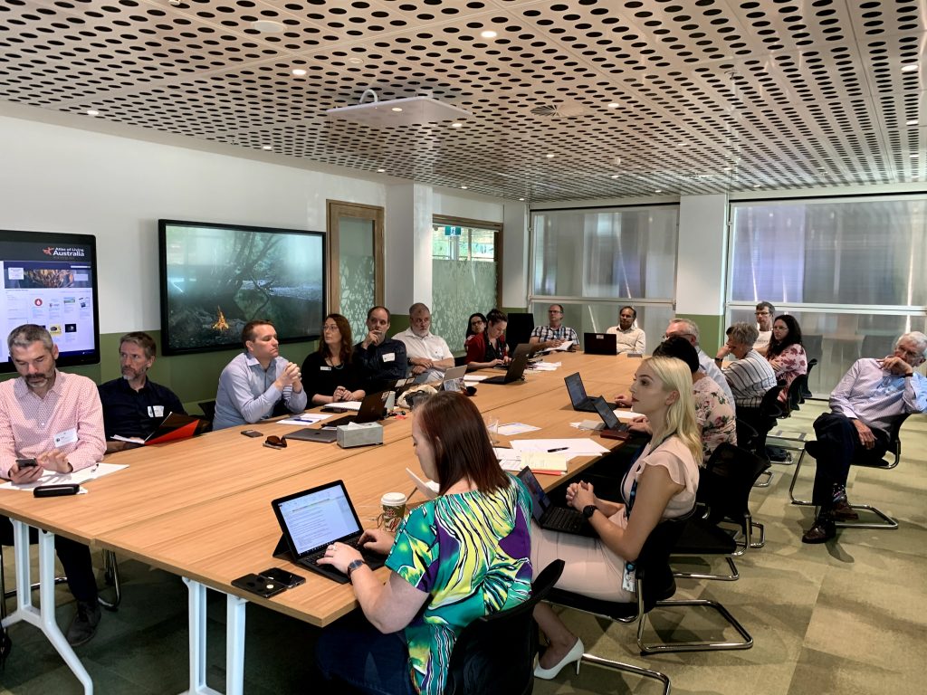 Participants of the Citizen Science Stakeholder Forum gathered around a large conference table with laptops open.