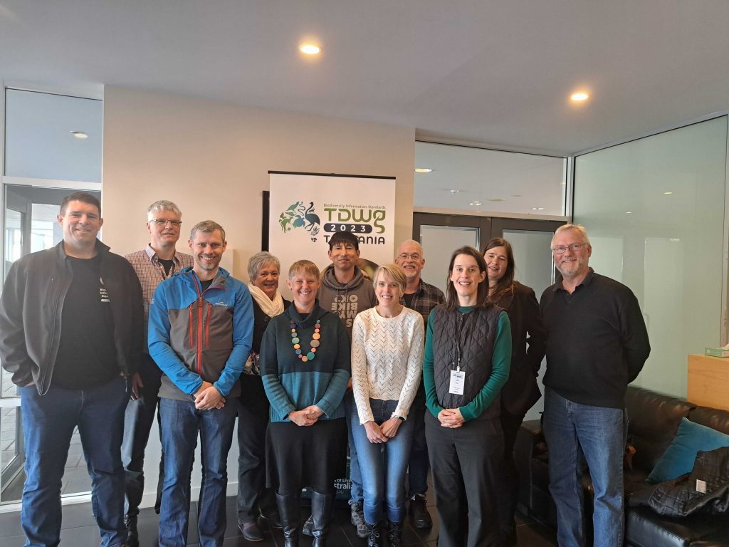 group of 11 people standing in front of a TDWG banner in a conference room